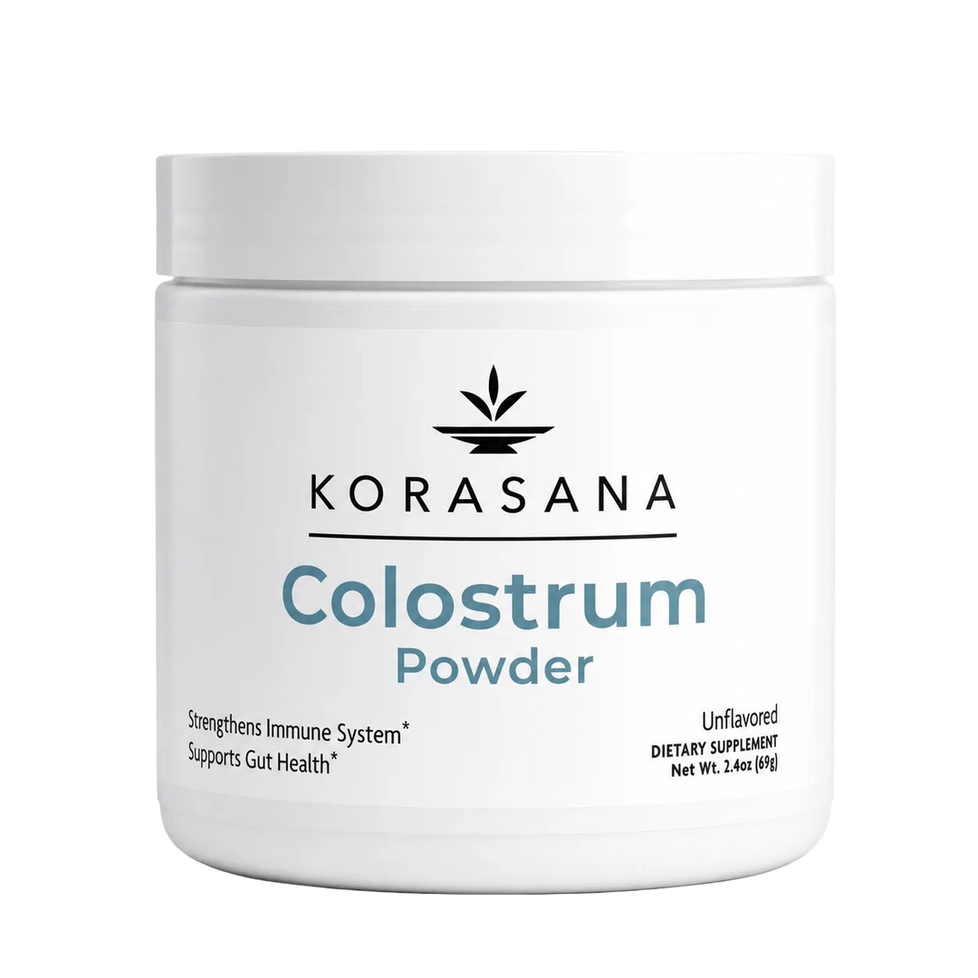 A white plastic jar of Korasana Colostrum Powder on a light gray background. The label features the brand name 'KORASANA' in black with a leaf logo above it, and 'Colostrum Powder' written in blue and gray text.