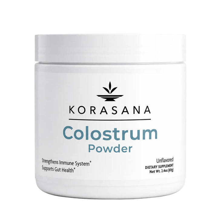 A white plastic jar of Korasana Colostrum Powder on a light gray background. The label features the brand name 'KORASANA' in black with a leaf logo above it, and 'Colostrum Powder' written in blue and gray text.